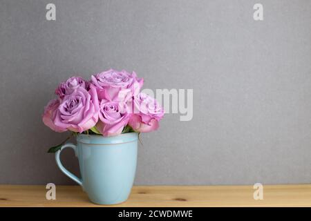 Interni domestici. Mazzo di fiori di rosa viola su tavolo di legno con sfondo grigio. Arrangiamento floreale, spazio copia Foto Stock