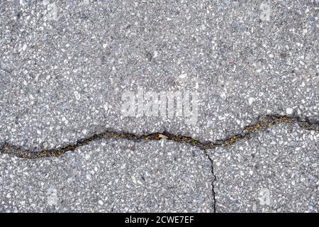 Un'area pavimentata con asfalto è vista dall'alto con una grande spaccatura che scorre attraverso di esso, e un'altra spaccatura perpendicolare più piccola sotto. Foto Stock