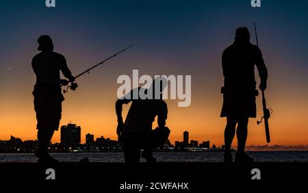 L'Avana, Cuba, Nov 19, 2017 - tre uomini visto in silhouette, pesca dal Malecon al tramonto Foto Stock