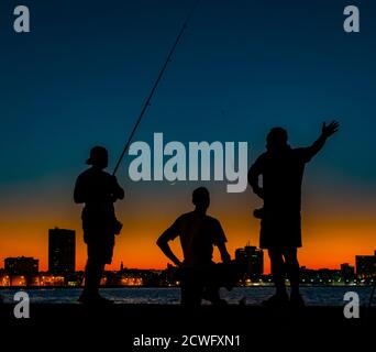 L'Avana, Cuba, Nov 19, 2017 - tre uomini visto in silhouette, pesca dal Malecon al tramonto Foto Stock