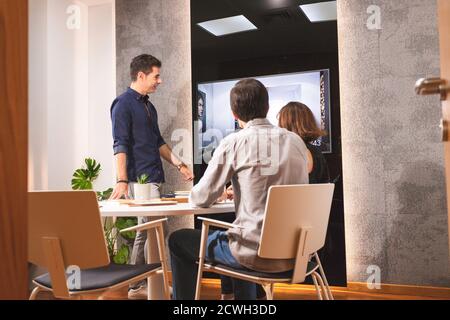 Tre giovani architetti discutono insieme all'interno di una sala conferenze il nuovo concetto di interior design per una presentazione del marchio. I giovani imprenditori lavorano Foto Stock