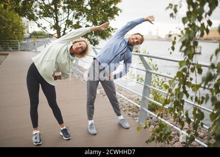Giovane coppia di abbigliamento sportivo in piedi e facendo esercizi di stretching nel parco Foto Stock