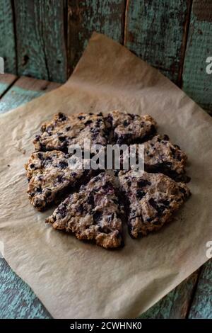 Focaccine rustiche di mirtillo su carta da forno e tagliere di quercia sopra vecchio sfondo di legno dipinto con copyspace Foto Stock