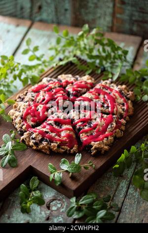 Focaccine di mirtillo con marmellata di lamponi su tavola di quercia con foglie di mirtillo su vecchio legno dipinto sfondo legno ad alto angolo Foto Stock