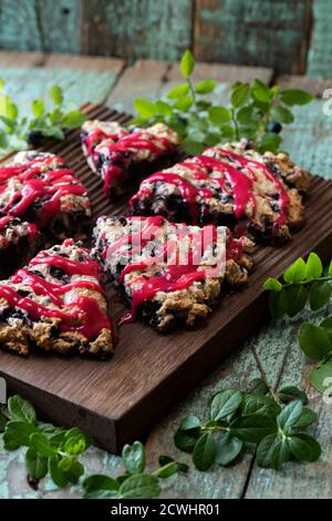 Focaccine di mirtillo con marmellata di lamponi su tavola di quercia con foglie di mirtillo su vecchio legno dipinto sfondo verticale Foto Stock
