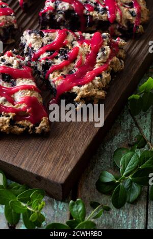 Focaccine di mirtillo con marmellata di lamponi su tavola di quercia con foglie di mirtillo su vecchio sfondo di legno dipinto da vicino Foto Stock