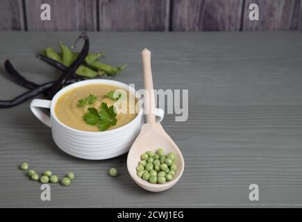 Piselli e fagioli schiacciati di zuppe in una tazza bianca su sfondo grigio di legno, accanto ad essa si trova un cucchiaio di legno con piselli . Inserire uno spazio per la copia Foto Stock