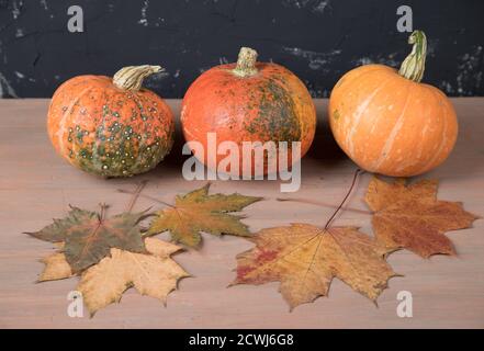 Tre zucche con foglie autunnali su sfondo di legno marrone Foto Stock