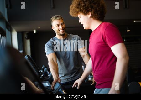 Giovane uomo in sovrappeso che esercita la palestra con personal trainer Foto Stock