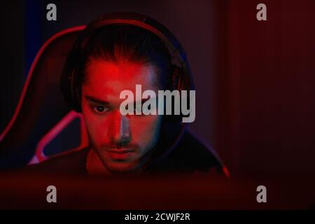 Sviluppatore di software giovane e serio in cuffie che lavora sul suo posto di lavoro si concentra sui suoi compiti Foto Stock