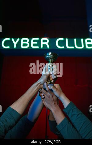Primo piano di un gruppo di giocatori che tengono insieme la coppa che hanno vinto il gioco del computer nella competizione di squadra Foto Stock