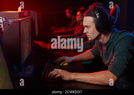 Giovane giocatore in cuffia guardando il monitor del computer e giocando giochi con altri giocatori in un club di computer Foto Stock
