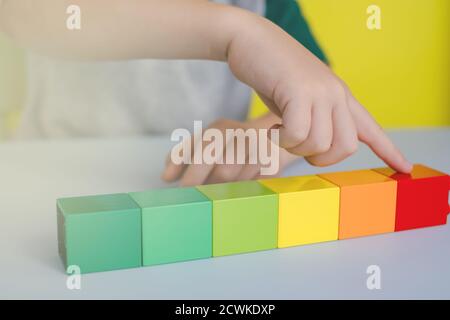 primo piano delle mani dei bambini che contano blocchi colorati in righe sul tavolo Foto Stock