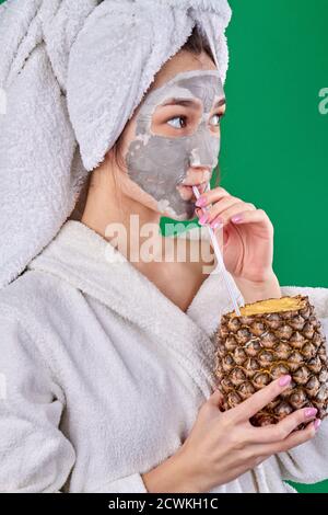 Ragazza con maschera di argilla è bere cocktail di ananas. Foto Stock