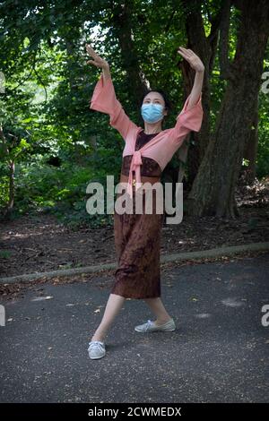 Circondato da alberi e foglie, un'elegante ballerina cinese americana danzano con musica folk tradizionale. In un parco a Queens, New York City Foto Stock