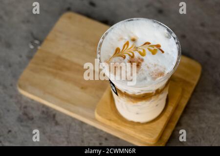 Caffè ghiacciato con crema di latte in un bicchiere di plastica è su un piattino di legno, fuoco selettivo, latte art Foto Stock