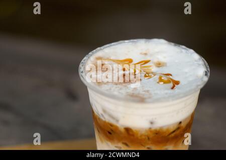 Il caffè ghiacciato con latte cremoso in un bicchiere di plastica è su un tavolo, fuoco selettivo, latte art Foto Stock