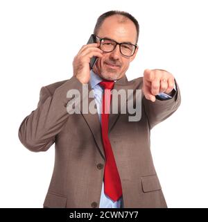 felice vecchio uomo d'affari che parla al telefono e che punta il suo dito sulla fotocamera su sfondo bianco Foto Stock