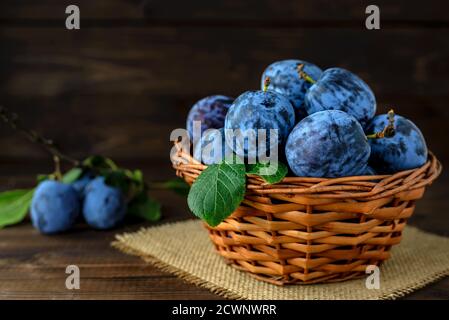 Prugne dolci in un cesto di vimini sul tavolo di legno con spazio per la copia del testo. Messa a fuoco selettiva. Foto Stock