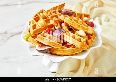 Cialde belghe con frutti di bosco freschi, pere, fichi su un piedistallo di torta bianca su un tavolo di marmo Foto Stock