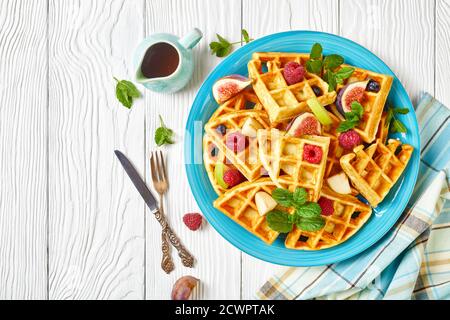 Cialde belghe con frutti di bosco freschi, pere, fichi su un piatto blu su un tavolo di legno bianco con sidro d'acero, piatto, spazio libero Foto Stock