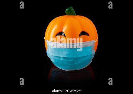 Zucca arancione di plastica di Halloween con maschera chirurgica blu, su sfondo nero con sopracciglia nere Foto Stock