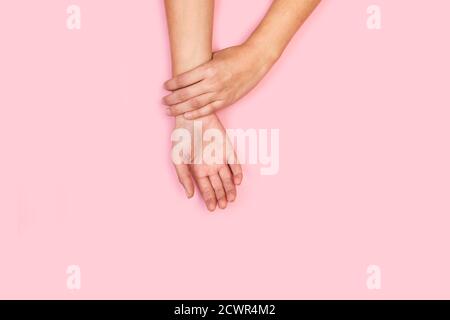 Mano della donna che tocca il proprio polso su uno sfondo rosa in una vista dall'alto Foto Stock