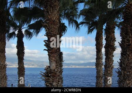 Vista panoramica sullo stretto di Messina da Reggio Calabria Con palme e lampioni vintage in primo piano Foto Stock