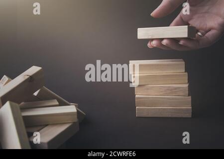 Tenere a mano un blocco di legno sotto la pila degli stessi blocchi. Immagine concettuale aziendale. Sfondo marrone con sole Foto Stock