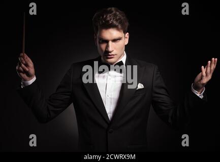 Giovane direttore d'orchestra che tiene un bastone in mano mentre guarda la fotocamera. Foto Stock