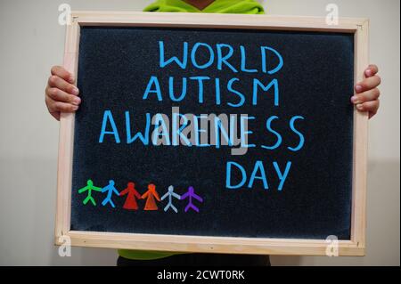 Giornata mondiale di consapevolezza dell'autismo. Ragazzo tenere lavagna con iscrizione blu. Foto Stock