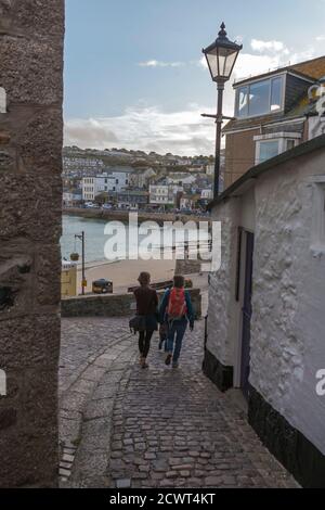 Due donne camminano lungo una corsia acciottolata in un villaggio di pescatori della Cornovaglia: Mount Zion, Downalong, St. Ives, Cornovaglia, Regno Unito. MODELLO RILASCIATO Foto Stock