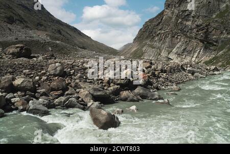 Il fiume scorre attraverso la valle profonda fiancheggiata da Himalaya e massi sotto il cielo blu in un giorno estivo luminoso vicino a Kaza, Himachal Pradesh, India. Foto Stock