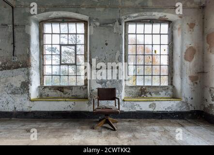 Vecchia sedia da ufficio tra grandi finestre in un rustico disusato mulino Foto Stock