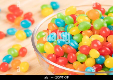 Primo piano di una deliziosa caramella Jelly Beans in un ciotola di vetro isolata su sfondo di legno Foto Stock