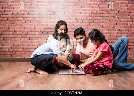 Giovane famiglia indiana di quattro giochi da tavolo come Scacchi, Ludo o snack e ladder a casa in quarantena Foto Stock