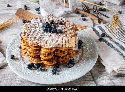 waffle fatti in casa appena sfornati a forma di cuore con mirtilli impilati su un piastra Foto Stock