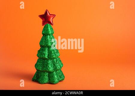 Miniatura modello Pino invernale in glitter verde con stella rossa sulla parte superiore su sfondo arancione. Natale, Natale Capodanno decorazione concetto Foto Stock
