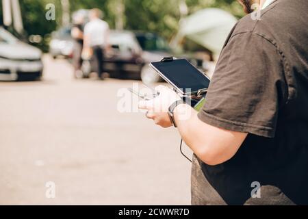 Un uomo nero controlla un drone utilizzando un telecomando e un tablet. È in piedi in un parcheggio auto Foto Stock