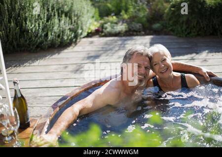 Ritratto felice coppia senior rilassarsi nella vasca idromassaggio al sole patio Foto Stock