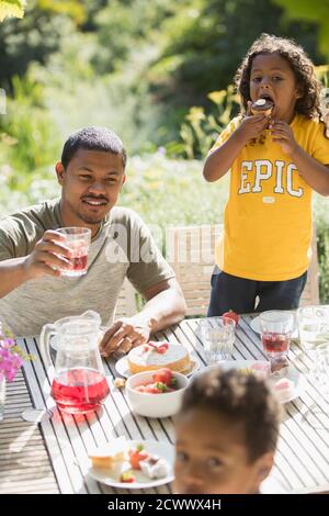 Padre e bambini gustano il pranzo in giardino sul luminoso patio estivo Foto Stock