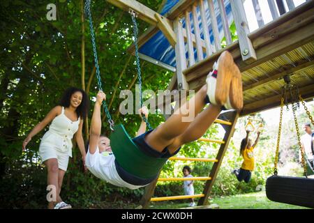 Famiglia felice dondolarsi e giocare nel parco giochi set in estate iarda Foto Stock