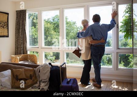 Affettuosa coppia anziana abbracciando al soleggiato finestra di affitto casa Foto Stock