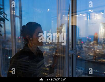 Donna d'affari premurosa che lavora tardi alla finestra dell'ufficio Foto Stock