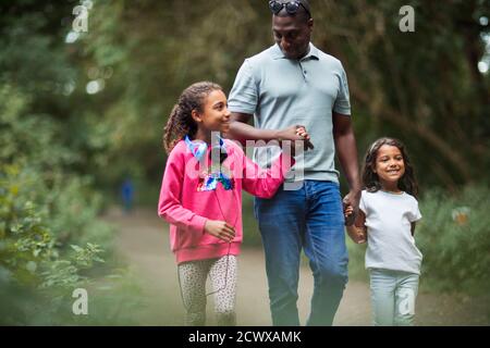 Felice padre e figlie che tengono le mani camminando sul sentiero del parco Foto Stock