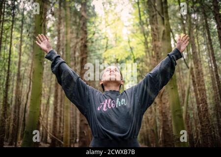 donna in una foresta con le sue braccia tese indossando una cima con aloha scritto su di esso. Foto Stock