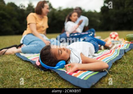 Ragazza con le cuffie che si rilassa e ascolta la musica durante il picnic coperta Foto Stock