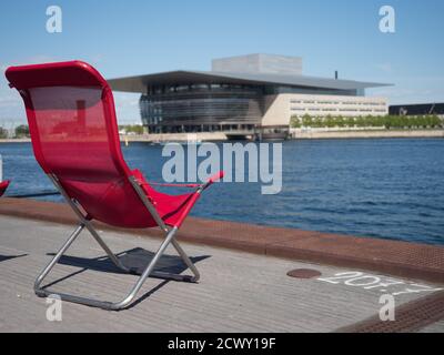 Copenhagen, Danimarca - 26 Aprile 2019: Rosso lettini con Copenaghen Opera House in background. Isola di Holmen Foto Stock