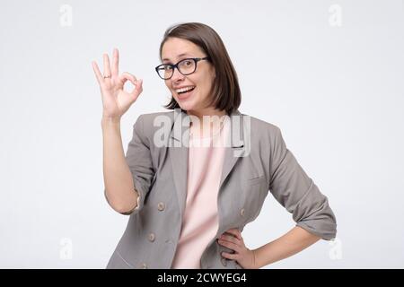 Giovane donna caucasica con occhiali che fa segno OK Foto Stock