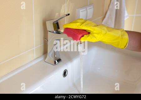 Lavabo e rubinetto per bagno con detergente in guanti di gomma gialla e spugna rosa. Concetto di casalinghi, pulizia, igiene, servizio di pulizia Foto Stock